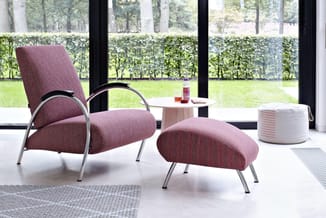 Roze gestoffeerde fauteuil met metalen frame en bijpassende voetenbankje in moderne kantoorruimte met groene tuin uitzicht.
