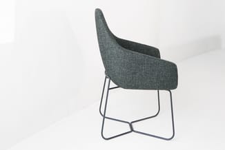 Grijze stof fauteuil met hoge gebogen rugleuning en metalen sled-onderstel in minimalistisch interieur.