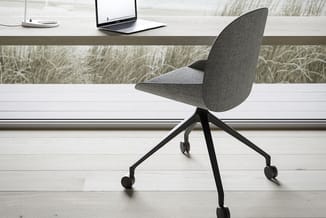 Grijze bureaustoel met wieltjes en zwart stalen onderstel aan witte bureau met laptop, voor raam met grasveld uitzicht.