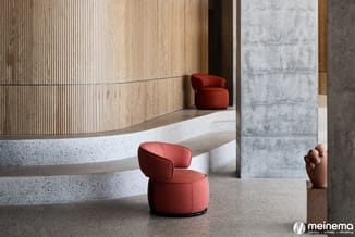 Ronde rode loungestoelen in een moderne kantoorruimte met houten wandpanelen, betonnen kolommen en terrazzo vloer.