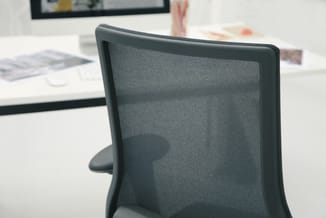 Grijze bureaustoel met mesh-rugleuning, gezien vanaf achteren in kantooromgeving met bureau en monitor.