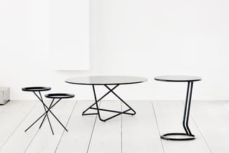 Collectie ronde tafels met zwart metalen onderstel en glasblad, in verschillende hoogtes en formaten, op witte houten vloer.