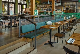 Modern restaurant met turquoise bankjes, houten tafels, zwarte stoelen en groene scheidingswand met meshpatroon.
