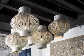 Drie hangende design-verlichtingsarmaturen met wit/beige geribde koepelvormen en gouden accenten in moderne kantoorruimte.