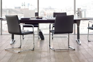 Modern kantoor met zwarte design stoelen met chromen onderstel aan zwarte tafel, laptops en grote ramen met stadsuitzicht.
