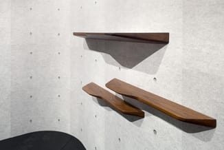 Houten wandplankjes in verschillende maten tegen witte pegboard-wand gemonteerd, bruine houttinten.