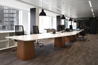 Modern kantoor met lange witte vergadertafel op houten poten, zwarte bureaustoelen, zwarte hanglampen en werkplekken met moni