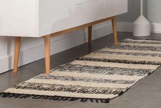 Minimalistisch interieur met wit dressoir op houten poten, zwarte vloer en gestreepte wollen loper in beige en zwart.