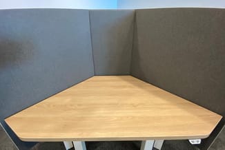 Hoekbureau met licht houten blad en grijze akoestische schermen in kantoorruimte.