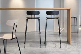 Houten vergadertafel met zwarte barkrukken en stoelen in modern kantoorinterieur met betonvloer.
