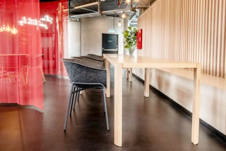 Moderne kantoorkantine met wit houten tafel, grijze stoel, rode glazen wand met neontekst, betonnen zuil en verlichting.