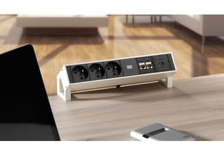 Witte bureau-stekkerdoos op houten tafel met drie stopcontacten, USB-poorten en "BASIC" markering, in kantooromgeving.