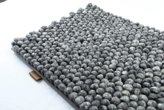 Grijze viltballen akoestiekmat op donkergrijs onderlaag met goudkleurig etiket, bovenaanzicht tegen witte achtergrond.