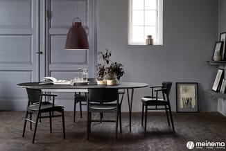 Vergaderruimte met ovale zwarte tafel, zwarte houten stoelen, bordeauxrode hanglamp, grijs geverfd muurwerk en natuurlijk lic