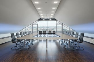 Moderne vergaderruimte op hoogste verdieping met zwarte gestoffeerde stoelen aan lange tafel, houten vloer en raampartijen me