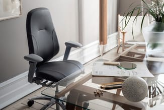 Zwarte ergonomische bureaustoel met armleuningen aan houten bureau in lichte kantoorruimte met planten en documenten.