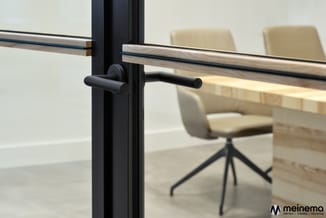 Zwart metalen trapleuning met houten greep in moderne kantoorruimte met beige stoelen en houten tafel op achtergrond.