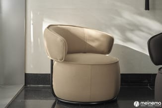 Creme kleurige ronde fauteuil met gebogen rugleuning en zwart metalen frame in minimalistische kantooromgeving.