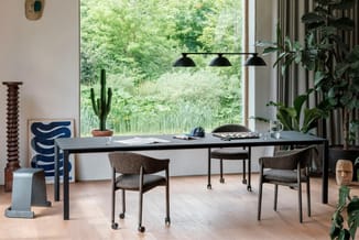 Zwarte vergadertafel met grijze stoelen op wielen in modern kantoor met grote ramen, groene planten en zwarte hanglampen.