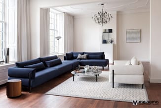 Moderne woonkamer met blauwe hoekbank, wit fauteuil, marmeren salontafel, houten bijzettafel, lichtgrijze vloerkleed en chrom