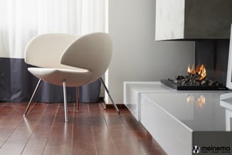 Moderne woonkamer met crèmekleurige design fauteuil op metalen poten, witte lage tafel en zwart haardmeubel met vuur. Houten