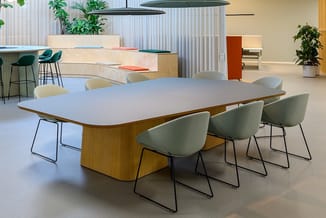 Moderne vergadertafel met afgeronde hoeken, houten onderstel en wit blad, omgeven door grijsgroene stoelen met zwart frame in