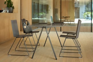 Moderne kantoorinrichting met grijze vergadertafel, vier grijze stoelen met metalen frame, laptop, kopjes en koptelefoon op t