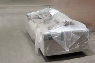 Verpakt kantoormeubel in plastic folie op betonvloer, vermoedelijk bureau of kast voor transport.
