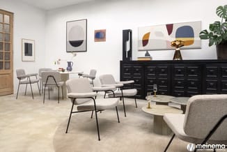 Moderne kantoorruimte met grijze stoelen met metalen poten, rond tafelwerk, zwart kastenstelsel, houten deur en abstract wand