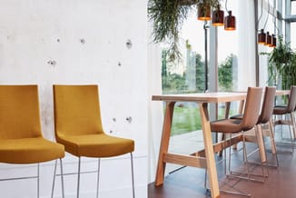 Modern kantoorinterieur met gele stoelen met metalen poten, houten eettafel, bruine barstoel, hanglampen en raamfront met uit