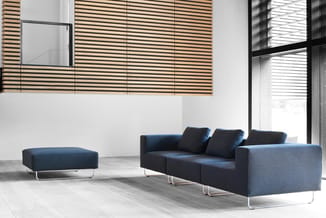Donkerblauwe loungebank met drie zitplaatsen en bijpassende ottoman op metalen poten in een modern kantoor met houten latten