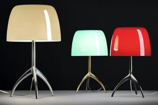 Drie tafellamp met gekleurde kunststof kappen (crème, mint, rood) op driepotige metalen voeten tegen zwarte achtergrond.