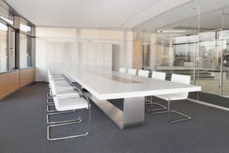 Moderne vergaderruimte met witte ovale vergadertafel, witte kantoorstoel en glazen wanden in licht interieur.