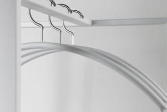 Witte garderoberek met drie metalen hangers aan aluminium rail tegen witte wand.