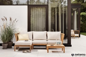 Houten loungeset met beige kussens op terras tegen grote ramen, met houten bijzettafel en potplanten.
