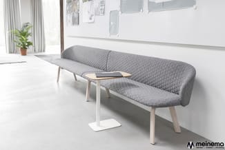 Grijze gebogen loungebank met gestoffeerd patroon in minimalistisch kantoor met houten tafeltje en witte vloer.
