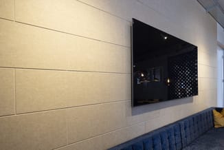 Wandpanelen in beige tint met horizontale stiksels, zwart wandmontage TV-scherm, donkerblauwe gestoffeerde bank met gele kuss