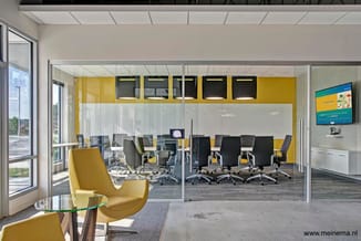 Moderne kantoorruimte met gele accent muren, glazen wanden, grijze bureaustoelen rond zwarte tafels, gele loungefauteuils met