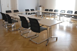 Moderne vergaderzaal met U-vormige tafelopstelling in licht hout, zwarte ergonomische bureaukstoelen met zijdelingse armleuni