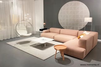Roze modulaire bank met ziteiland in modern ingerichte showroomruimte, met grijs accent muur, rond wandpaneel, hangende stoel