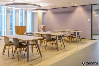 Modern kantoorruimte met twee houten vergadertafels, grijze en roze stoelen, roze wand, ronde hangende verlichting en grote r