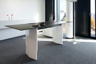 Modern kantoor met zwart-witte design bureau, wit onderstel met opbergruimte, grijze tapijttegel, grote ramen en minimalistis