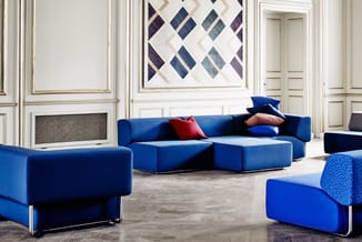 Blauwe modulaire loungeset in moderne kantoorruimte met witte wandpanelen, grafisch artwork en grijze vloer.