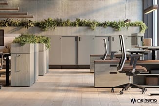 Modern kantoor met lichte houten bureaus, ergonomische stoelen, lichtgrijze kasten en groene plantenbakken aan betonnen wand.