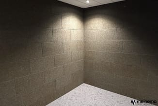 Lege belcel met grijsbruine tegeltegels aan wanden, lichte vloer, ingebouwde verlichting, hoekopstelling.