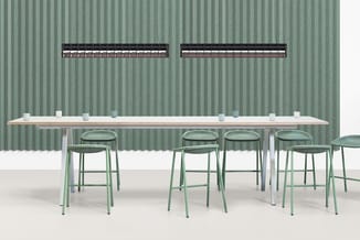 Lange houten bartafel met grijze ondersteuning, vier groene barstoelen, groene golfplaten wand, twee dakramen.
