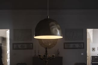 Zwarte hanglamp met dome vorm en verlichte binnenkant boven goudkleurige kandelaar in moderne kantoorruimte met donkere wande