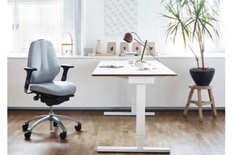 Kantoor werkplek met grijze ergonomische bureaustoel, wit bureaublad, witte onderkast, wandplank met decoratie en plant in zw
