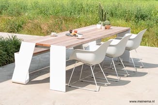 Moderne tuintafel met houten blad en witte trapeziumvormige poten, met vier witte ergonomische stoelen op betonnen terras, gr