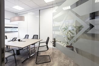 Moderne vergaderruimte met witte vergadertafel, zwarte kantoorstoelen, glazen wanden, hanglamp en plant op trap.
